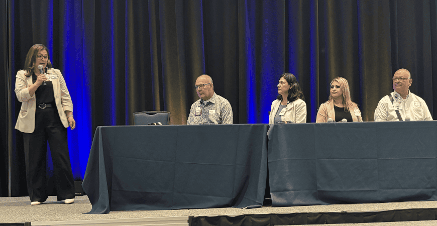 Panel session with the moderator standing and holding a mic and four panelists seated